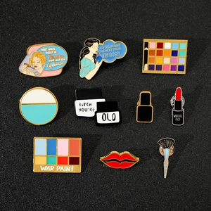 Macro shot of colorful enamel makeup pins featuring eye shadow palettes and lipstick on black