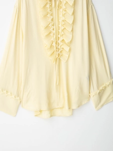 Detail of light yellow long sleeve shirt with ruffled collar and pleated front textures