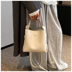 Detail of cream leather bucket bag with top handle and logo on a lifestyle model