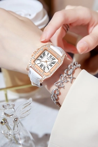 Detail of a square rose gold watch with rhinestones and white leather strap on wrist