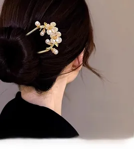 Détail d'une épingle à cheveux dorée en U avec fleurs blanches et perles sur chignon