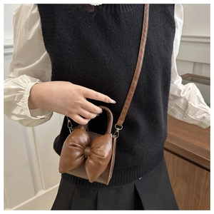 Brown mini crossbody bag with large bow detail shown on model for size perspective