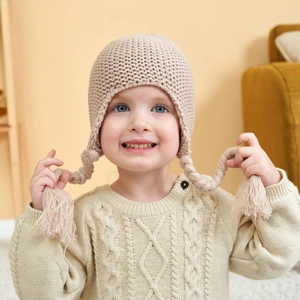 Beige knitted baby hat with ear flaps and braids for winter warmth and comfort