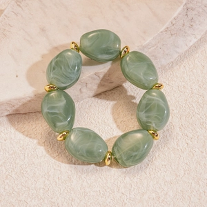 Detailed view of sage green acrylic marble beads with golden spacers on stone surface