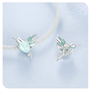 Macro detail of silver hummingbird charm with blue and green enamel and small gemstones