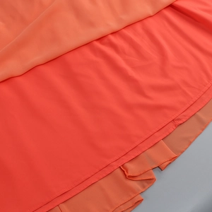 Dettaglio dell'orlo in chiffon arancione a strati e delle cuciture sull'abito lungo