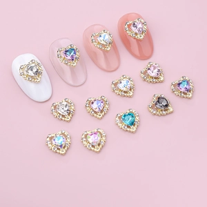 Close-up of heart-shaped crystal nail charms with gold metal frames for DIY manicure art