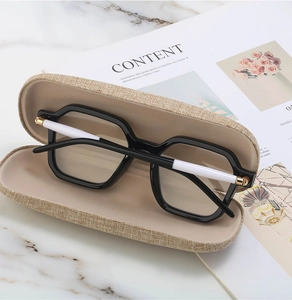 Detail of square black sunglasses with white arms in a beige woven case on marble surface
