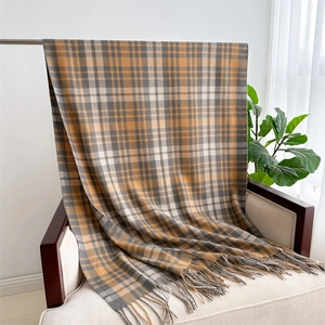 Close-up of a soft yellow and grey plaid scarf with tassels draped over a chair