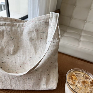 Dettaglio di una borsa tote in tela beige con puntini colorati ed etichetta