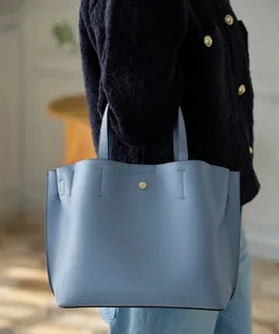 Detail of light blue textured leather tote bag with circular gold buckle on a model