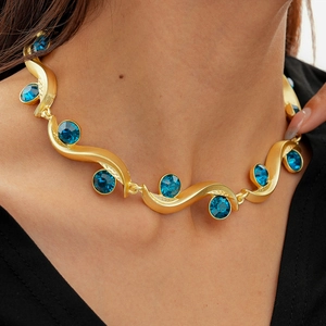 Close-up of golden wave necklace with blue crystals on a model for a luxury look