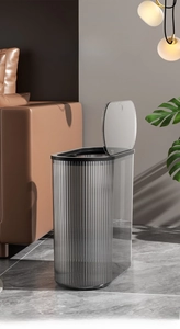 Macro detail of a slim dark grey textured trash bin placed near a brown leather sofa