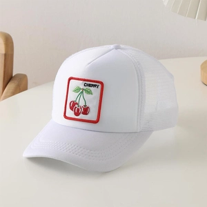 Dettaglio del cappellino trucker bianco con ricamo di ciliegie su un tavolo bianco
