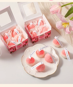 Detailed view of pink handmade strawberry candles in a gift box with floral accents