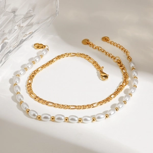 Close-up of double-layer gold Figaro chain and white pearl anklet with lobster clasp