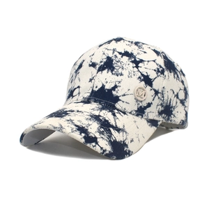 Close-up of a tie-dye baseball cap featuring a round metal badge with the letter M