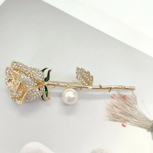 Detailed close-up of golden rose brooch with rhinestones, pearl, and green enamel leaves