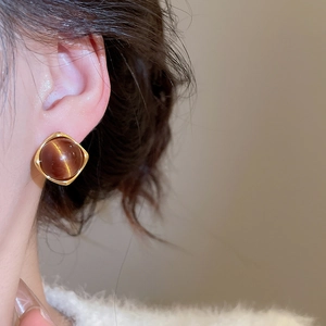 Macro detail of square gold stud earring with round brown tiger eye stone on model