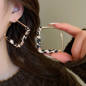 Detail shot of oversized square gold earrings featuring leopard print leather accents
