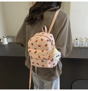 Pink corduroy mini backpack featuring red strawberry patterns and a cute plush charm