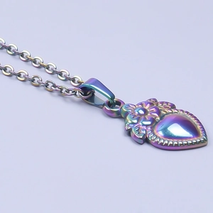 Macro detail of heart pendant with 18k rainbow plating and floral relief patterns