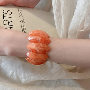 Detail of orange and white marble texture acrylic elastic bracelet on model wrist
