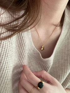 Detail view of a golden bean pendant necklace and black gemstone ring on a woman
