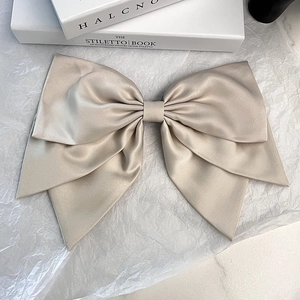 Elegant large beige satin bow hair clip placed on books for a minimalist Korean style