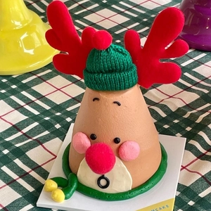 Close-up of reindeer Christmas cake topper with green knit hat and scarf on a white base