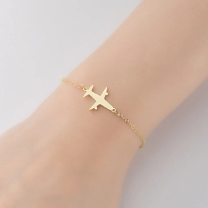 Detail of a minimalist gold airplane charm bracelet on a female wrist for travel style