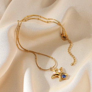 Detail view of gold starfish pendant with blue gemstone and pearls on a double-layered chain