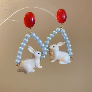 Détail de boucles d'oreilles lapin avec résine rouge et perles bleues triangulaires