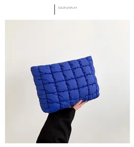 Detailed side view of a quilted royal blue puffy clutch bag held by a hand