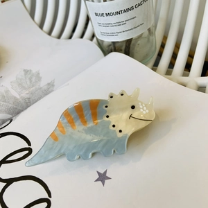 Detail shot of a cute acrylic dinosaur hair claw clip with blue and orange stripes