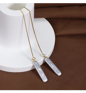 Detail of long gold box chain earrings featuring baroque iridescent stick pearls