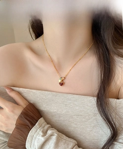 Detail of 18k gold plated necklace with a red heart pendant worn on a model's neck