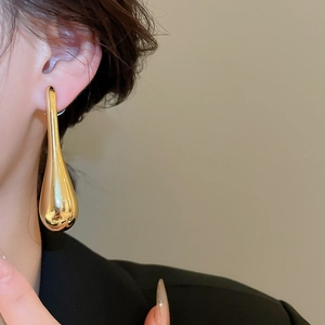 Close-up of golden teardrop pendant earring on model with high-shine metallic finish