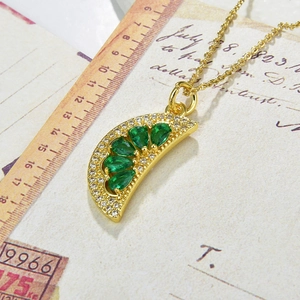 Detail of gold watermelon pendant with green zircons on vintage paper background