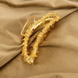Detail shot of banana-shaped hair claw with gold metal frame and yellow crystal stones