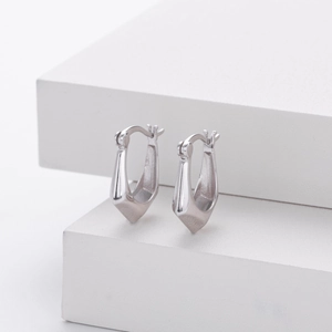 Macro shot of silver geometric hoop earrings on a minimalist white architectural pedestal