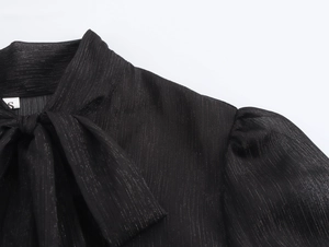 Détail du col d'une robe en mousseline noire avec nœud et texture de soie argentée