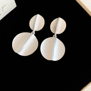 Close-up of geometric matte silver earrings with double circular origami design on black background