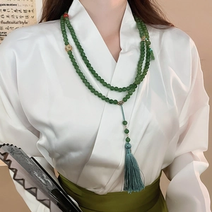 Détail d'un long collier de perles chinoises avec perles de jade vert et pompons en soie