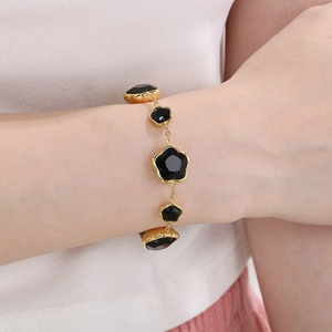 Gros plan d'un bracelet trèfle doré en titane avec pétales noirs porté au poignet