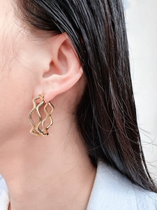 Macro detail of gold wave double-layered earrings with snakeskin texture on model