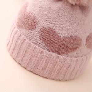 Close-up of pink knit baby hat with heart patterns and soft faux fur pom-pom detail