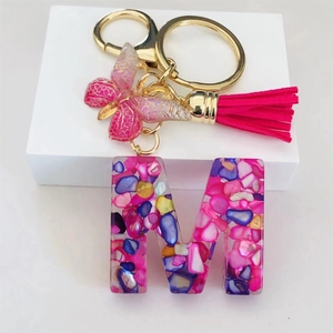 Detail of resin letter M keychain with rose red tassel and gold butterfly charm