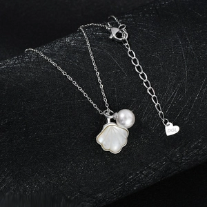 Detailed view of silver necklace with shell and pearl charms on black leather background