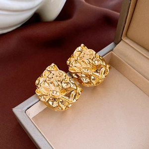 Detailed close-up of golden irregular textured flower earrings on a velvet display